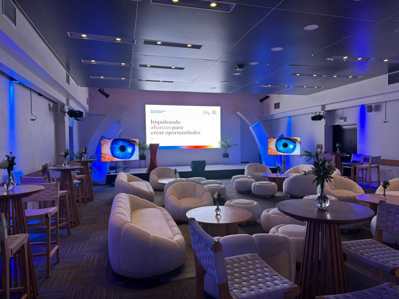 Salón preparado para un foro clínico con escenario, pantallas y luz azul